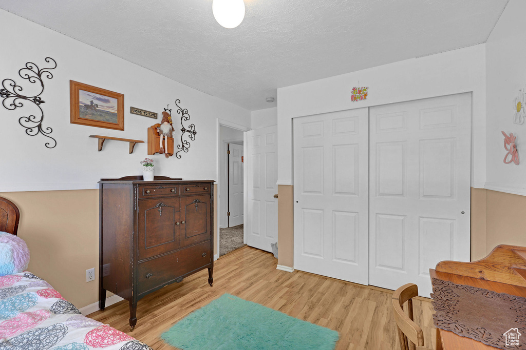 Bedroom with light wood-style floors, a closet, a textured ceiling, and baseboards