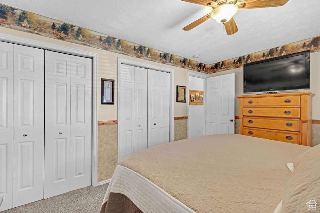 Bedroom featuring multiple closets, carpet flooring, a textured ceiling, a wainscoted wall, and ceiling fan