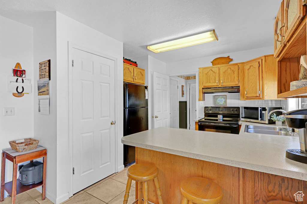 Kitchen featuring black appliances, under cabinet range hood, a peninsula, a sink, and light countertops