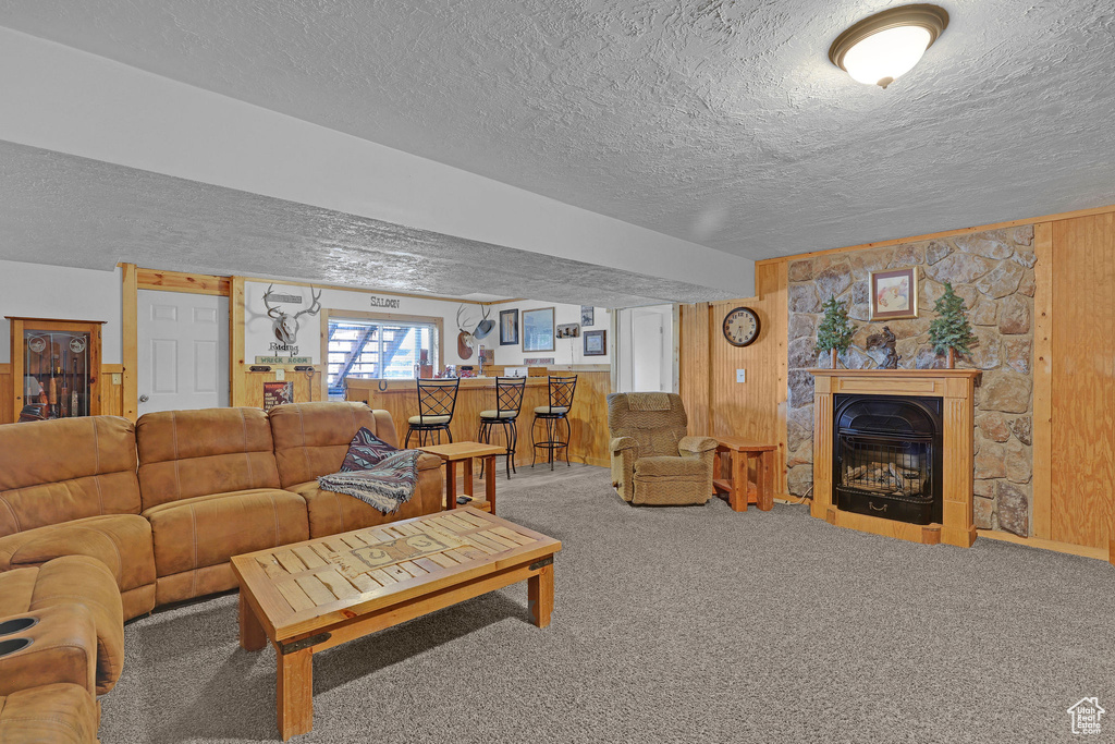 Living room with a textured ceiling, wood walls, carpet flooring, and a glass covered fireplace
