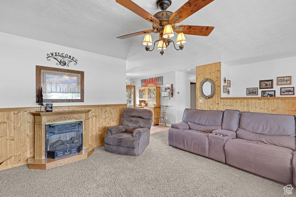 Living room with wood walls, a ceiling fan, wainscoting, carpet floors, and a textured ceiling