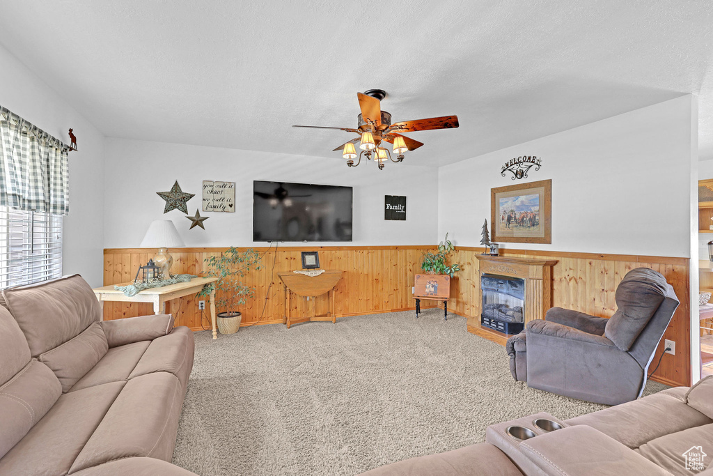 Living area with wainscoting, wooden walls, carpet, ceiling fan, and a fireplace