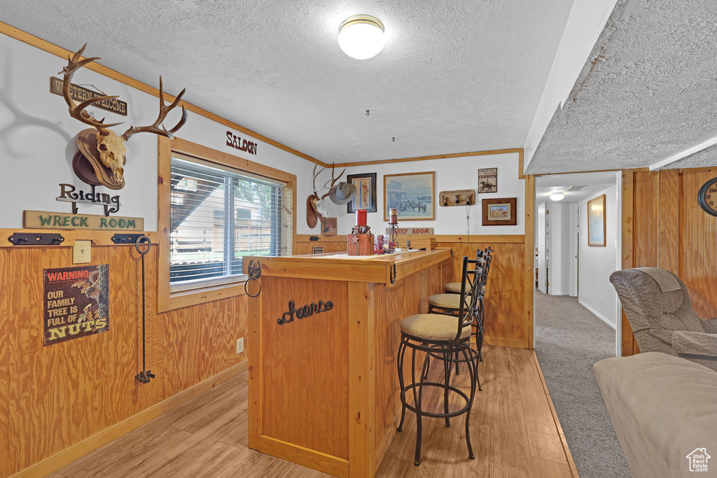 Indoor dry bar with a textured ceiling, wood walls, light wood-type flooring, wainscoting, and baseboards
