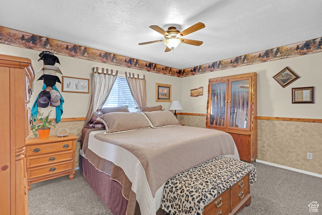 Bedroom featuring a textured ceiling, carpet floors, a wainscoted wall, and a ceiling fan