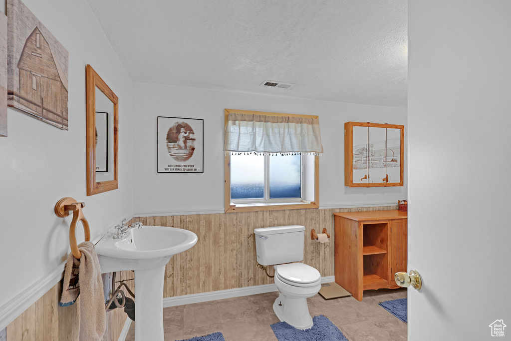 Bathroom with toilet, wainscoting, wooden walls, and a textured ceiling
