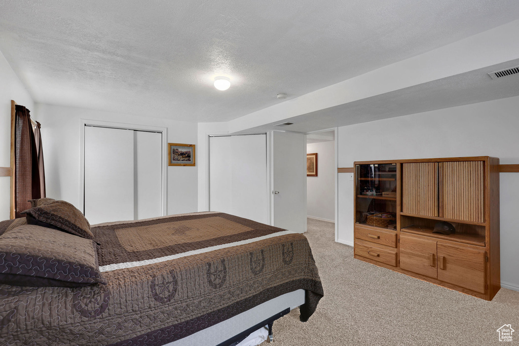 Bedroom featuring light carpet, baseboards, and a textured ceiling