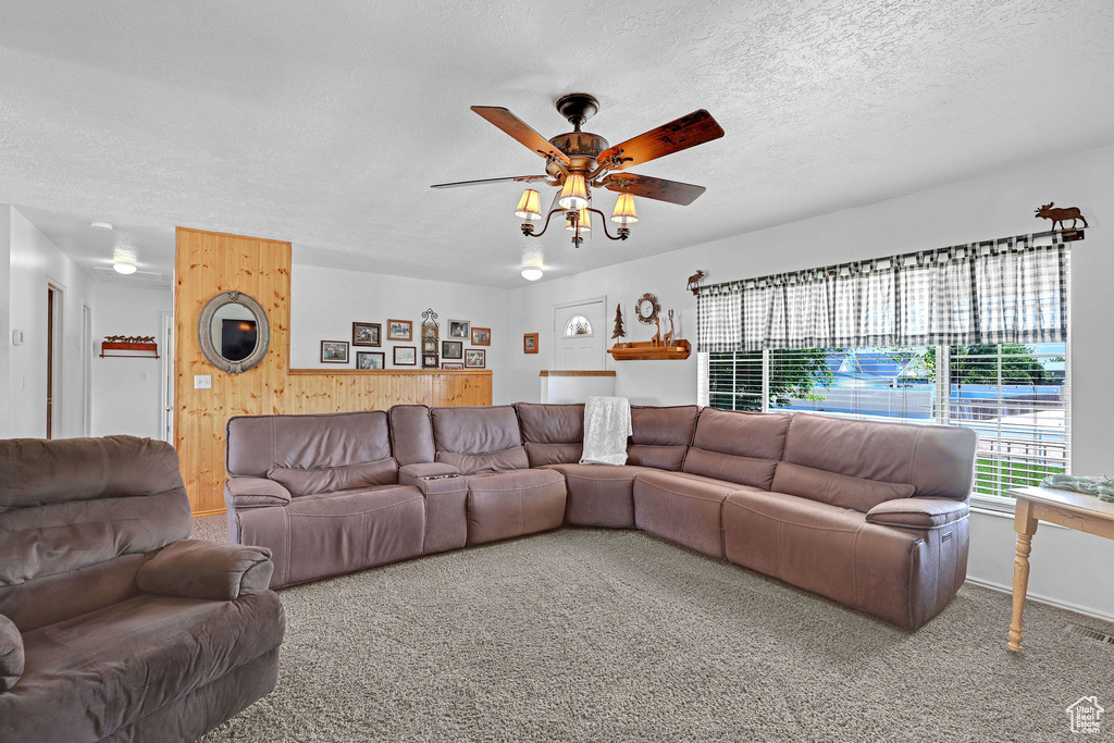 Living area featuring wood walls, a textured ceiling, ceiling fan, and carpet