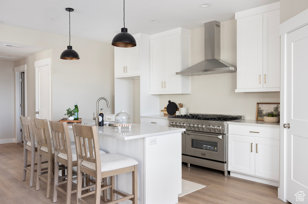 Kitchen with wall chimney range hood, high end range, light wood finished floors, light countertops, and white cabinetry
