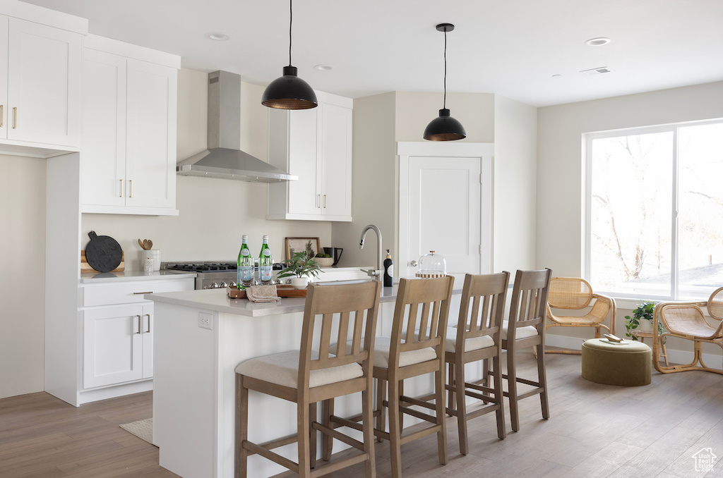 Kitchen featuring wall chimney exhaust hood, light wood-style flooring, light countertops, white cabinetry, and recessed lighting