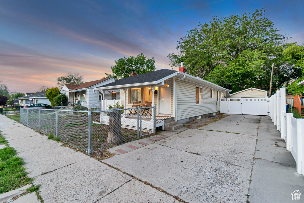 Shotgun-style home with a gate, covered porch, a chimney, and a detached garage