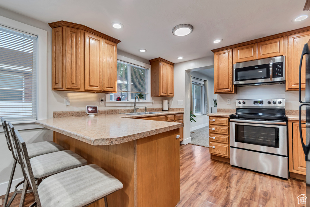 Kitchen with appliances with stainless steel finishes, a sink, light wood finished floors, a peninsula, and a kitchen breakfast bar