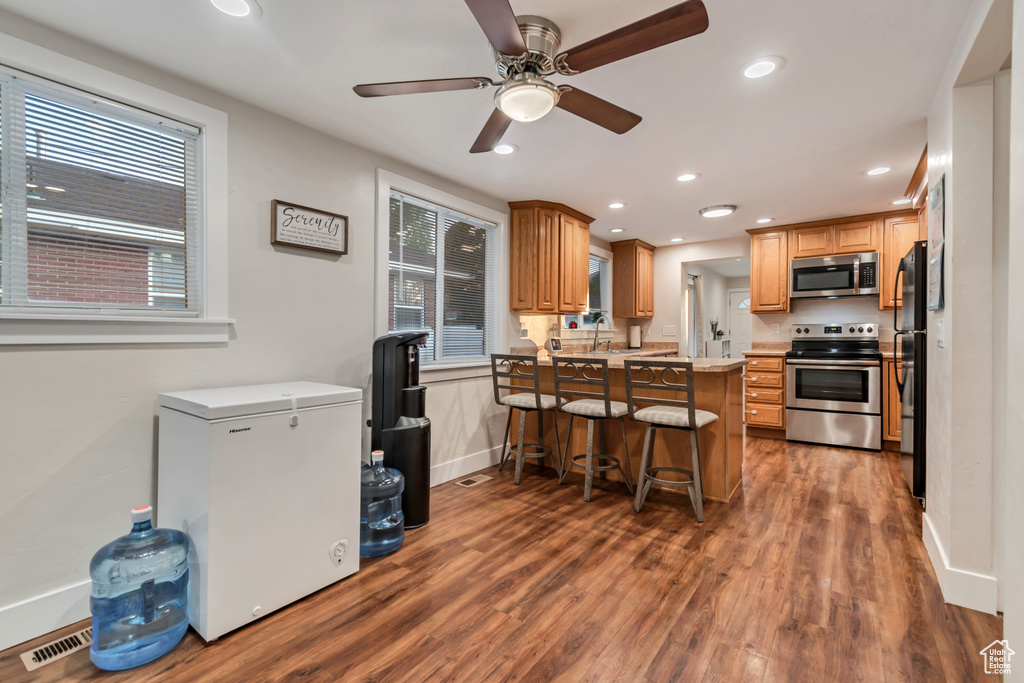 Kitchen with stainless steel appliances, a peninsula, recessed lighting, a breakfast bar area, and dark wood-type flooring
