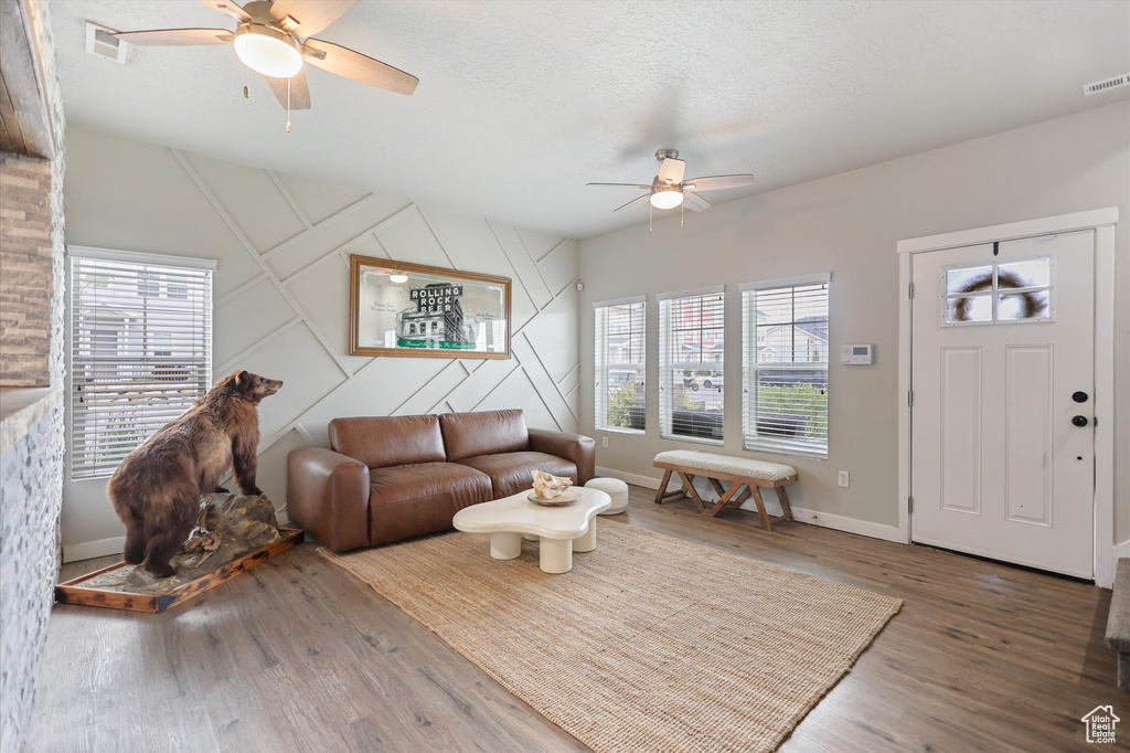 Living area featuring ceiling fan, plenty of natural light, wood finished floors, baseboards, and a textured ceiling