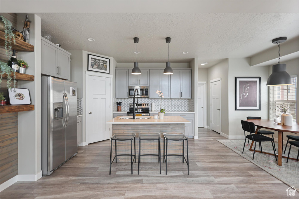 Kitchen with appliances with stainless steel finishes, baseboards, light countertops, decorative backsplash, and light wood-style floors