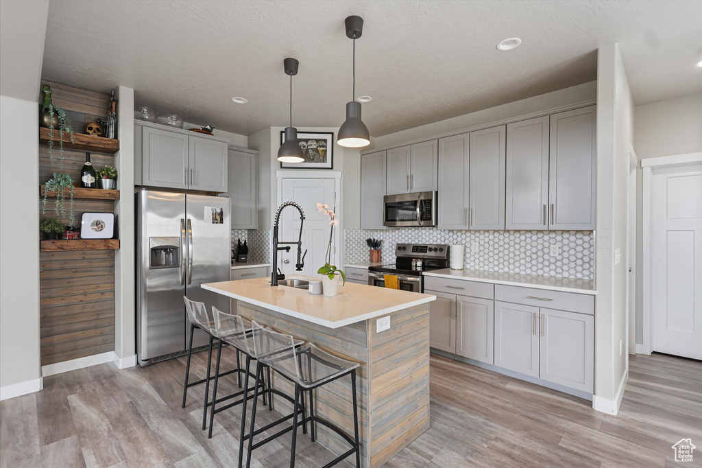 Kitchen featuring appliances with stainless steel finishes, gray cabinets, an island with sink, a breakfast bar, and tasteful backsplash
