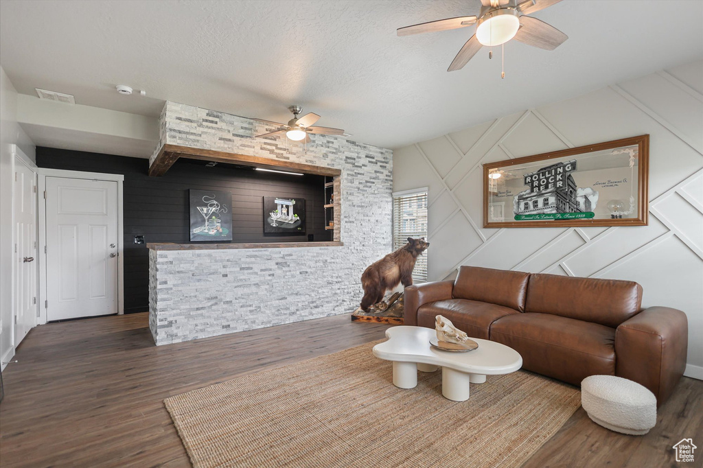 Living room featuring a ceiling fan, wood finished floors, a decorative wall, and a textured ceiling