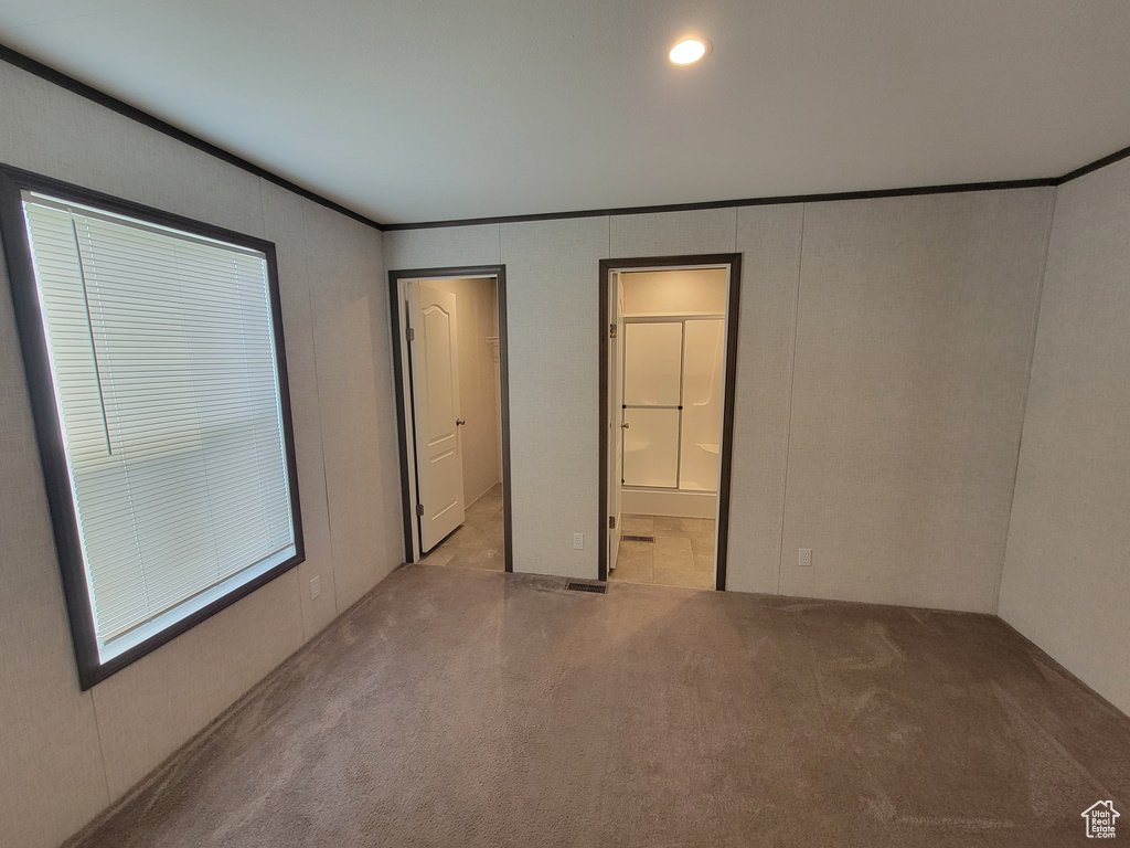 Unfurnished bedroom featuring crown molding, carpet floors, a decorative wall, and ensuite bath