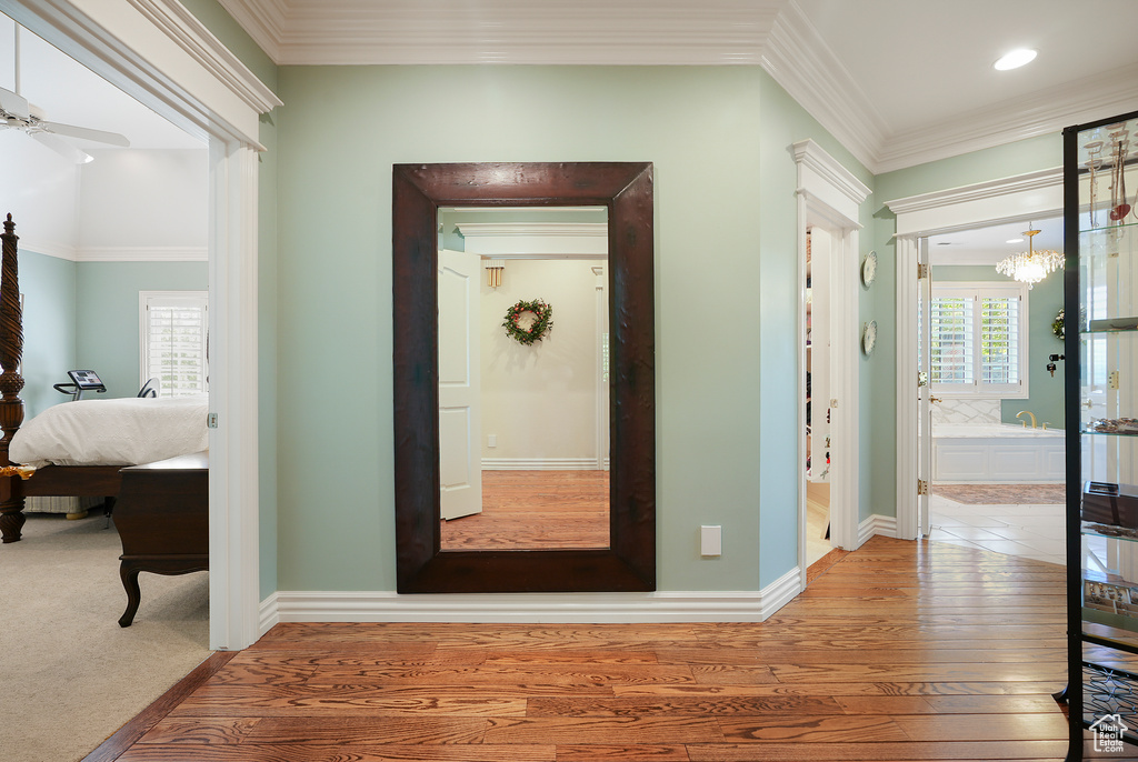 Hallway with healthy amount of natural light, wood-type flooring, a chandelier, crown molding, and baseboards