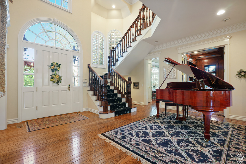 Entryway featuring hardwood / wood-style flooring, stairs, crown molding, baseboards, and a high ceiling