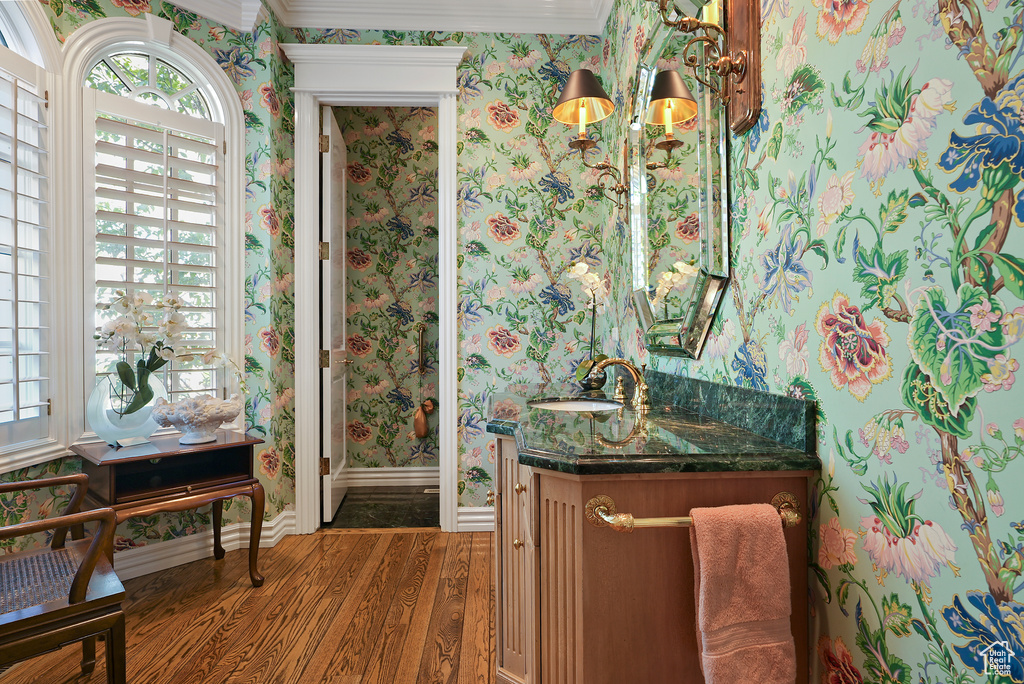 Bathroom with wallpapered walls, wood finished floors, vanity, baseboards, and healthy amount of natural light