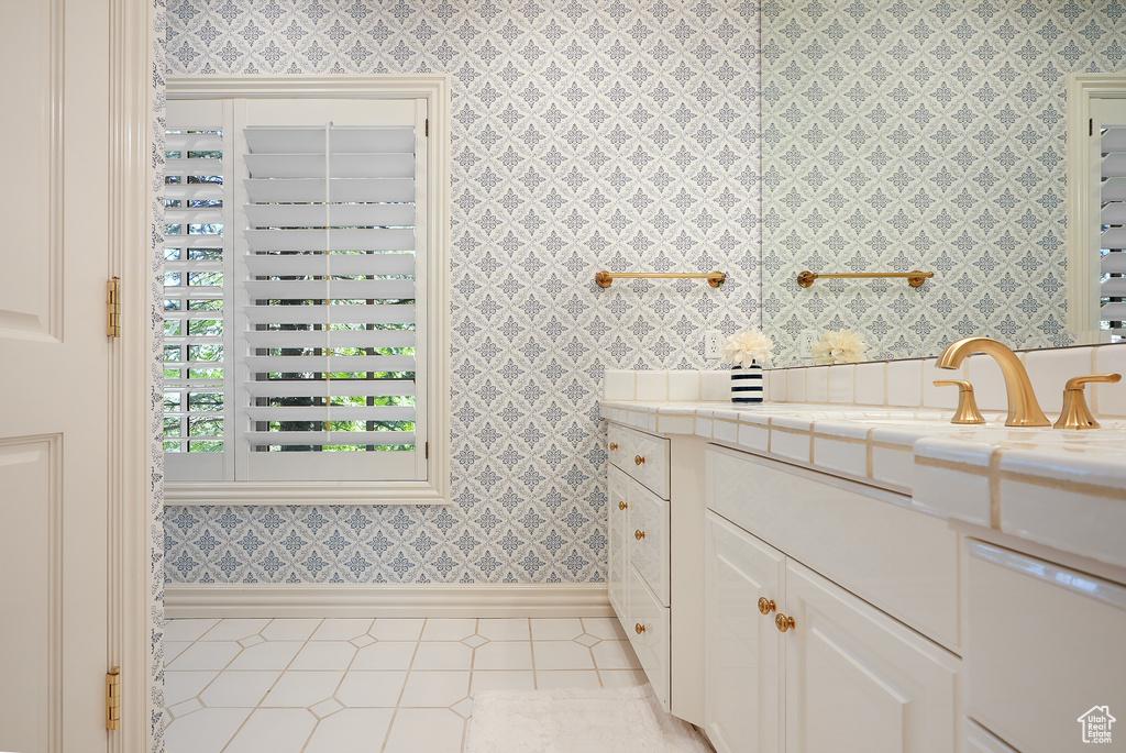 Bathroom with wallpapered walls, baseboards, vanity, and tile patterned flooring