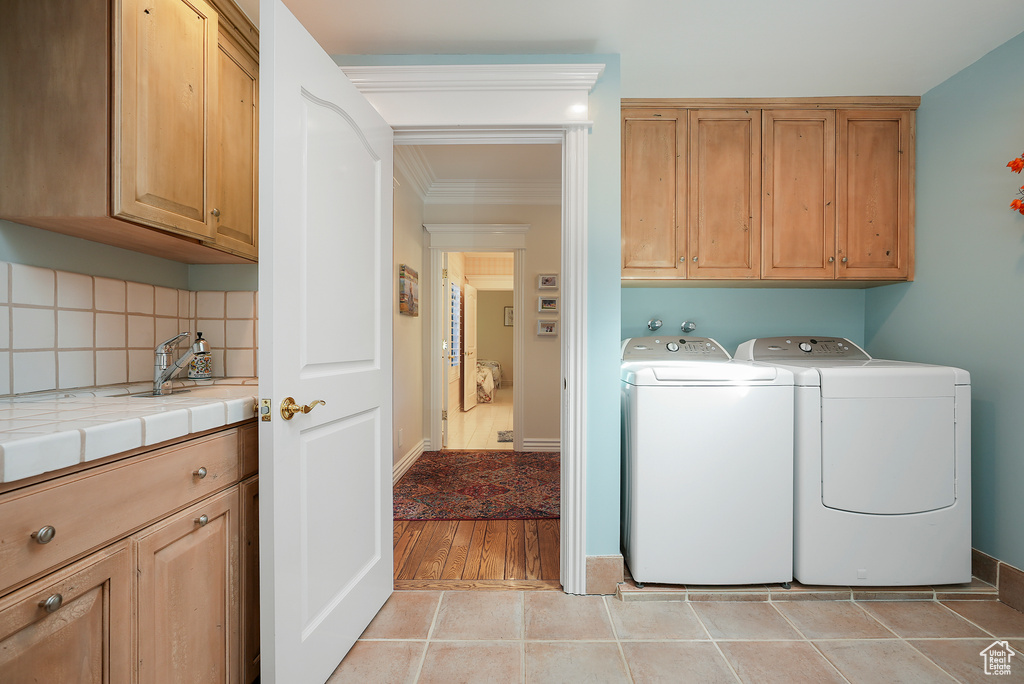 Laundry room with cabinet space, washing machine and clothes dryer, ornamental molding, and light tile patterned flooring