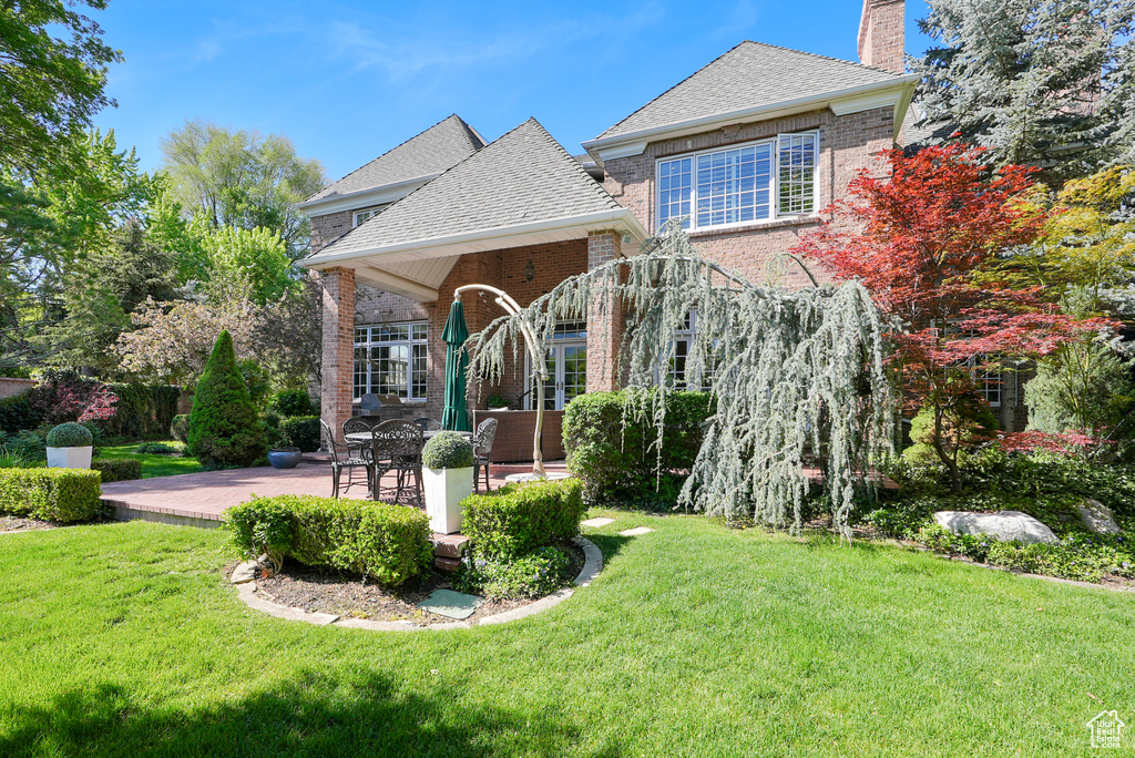 Back of property featuring brick siding, a chimney, and a lawn