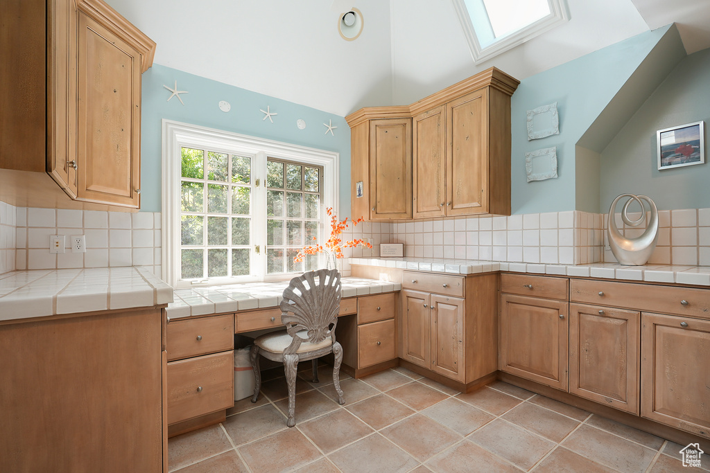 Kitchen with backsplash, tile counters, vaulted ceiling, a skylight, and light tile patterned flooring