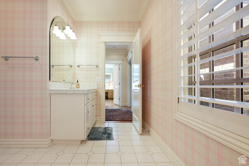 Bathroom with wallpapered walls, crown molding, vanity, baseboards, and tile patterned floors