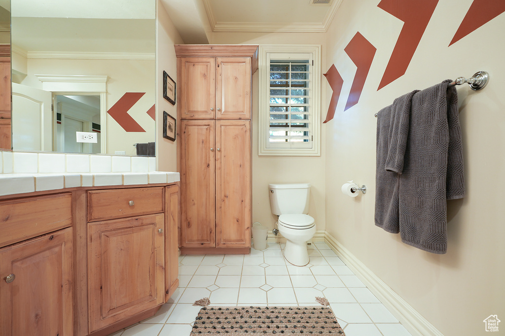 Bathroom featuring toilet, vanity, crown molding, baseboards, and tile patterned floors