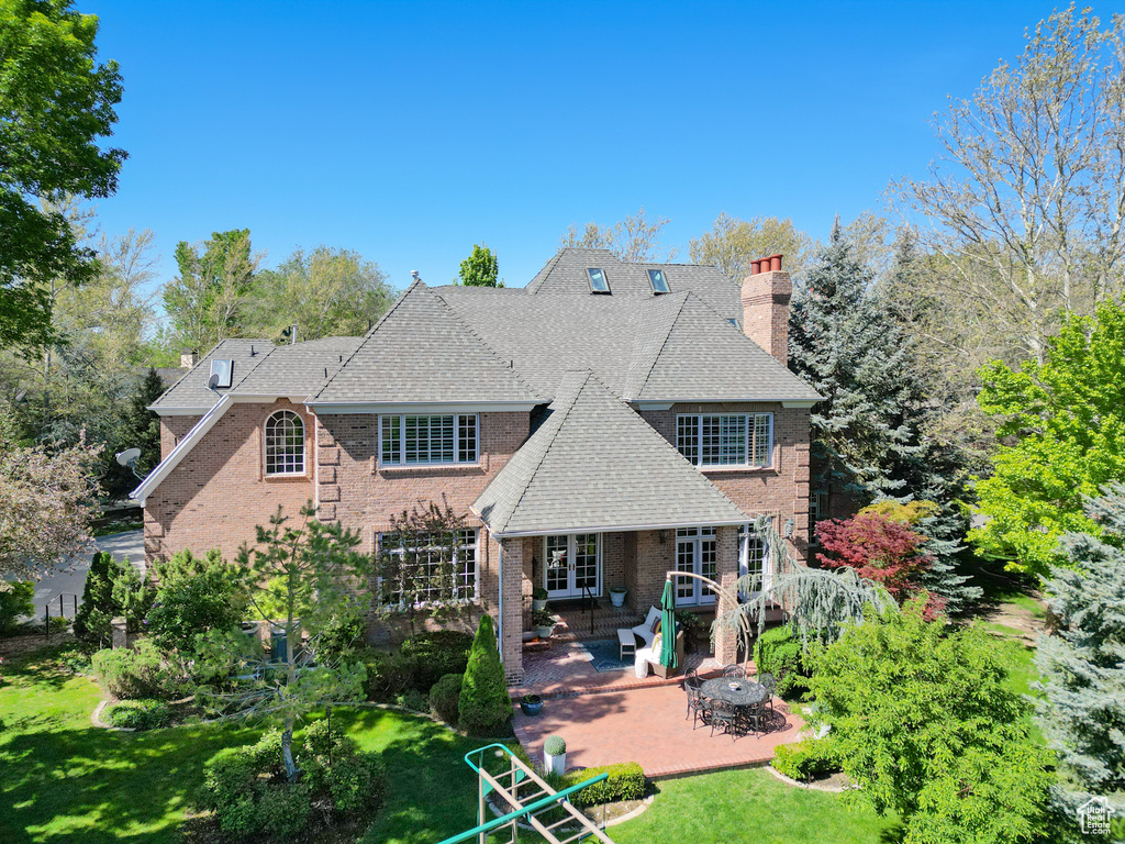 Back of property with a chimney, a patio, a yard, brick siding, and french doors