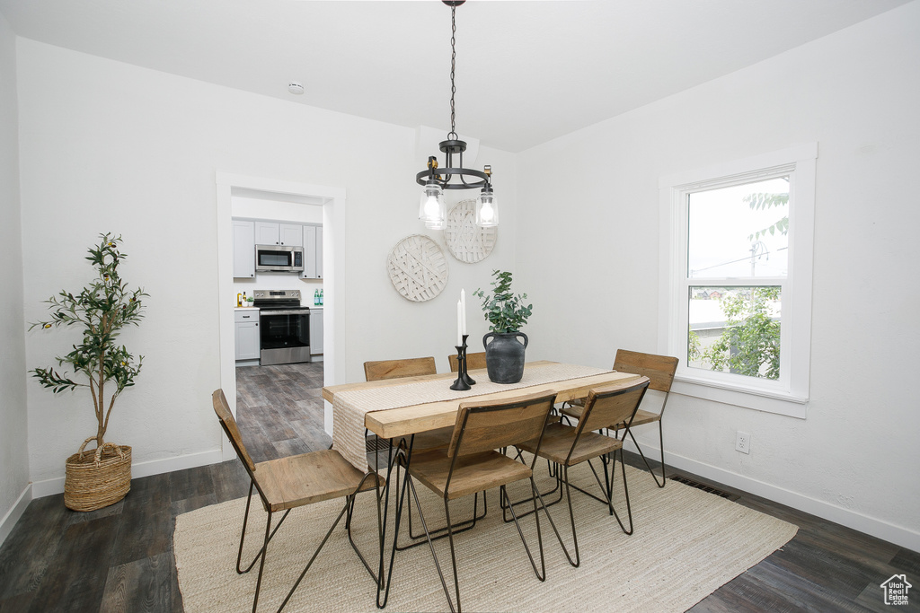 Dining area featuring dark wood-style flooring, a chandelier, and baseboards