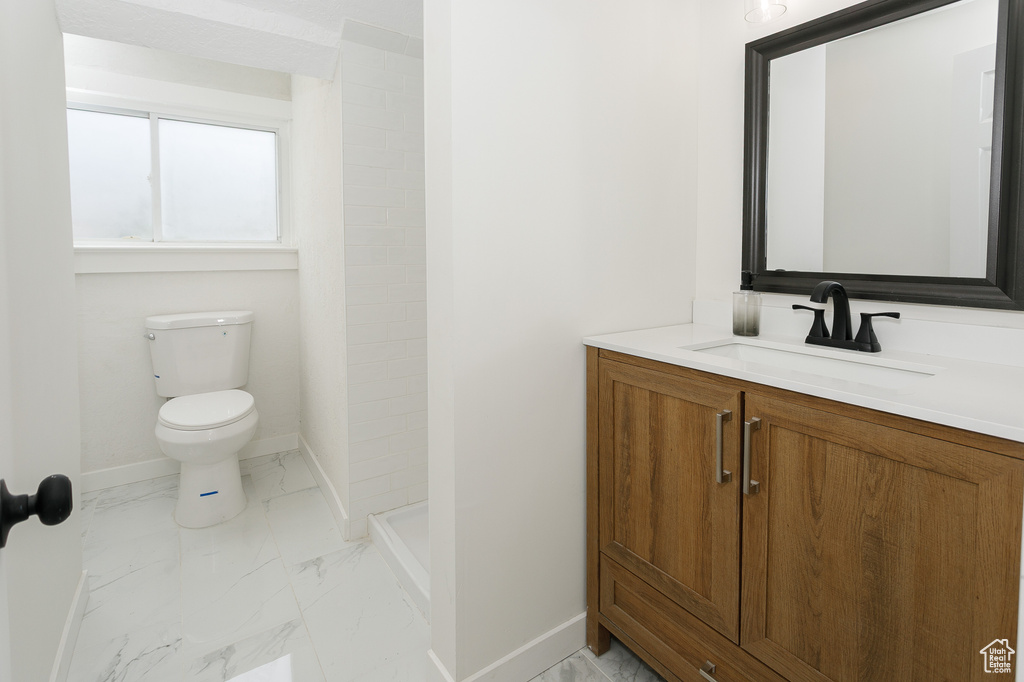 Bathroom featuring baseboards, marble look tiles, toilet, vanity, and a shower