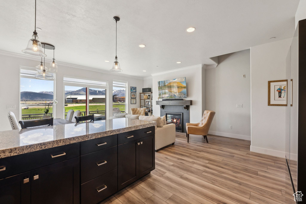 Kitchen with ornamental molding, dark cabinetry, baseboards, a glass covered fireplace, and light wood finished floors