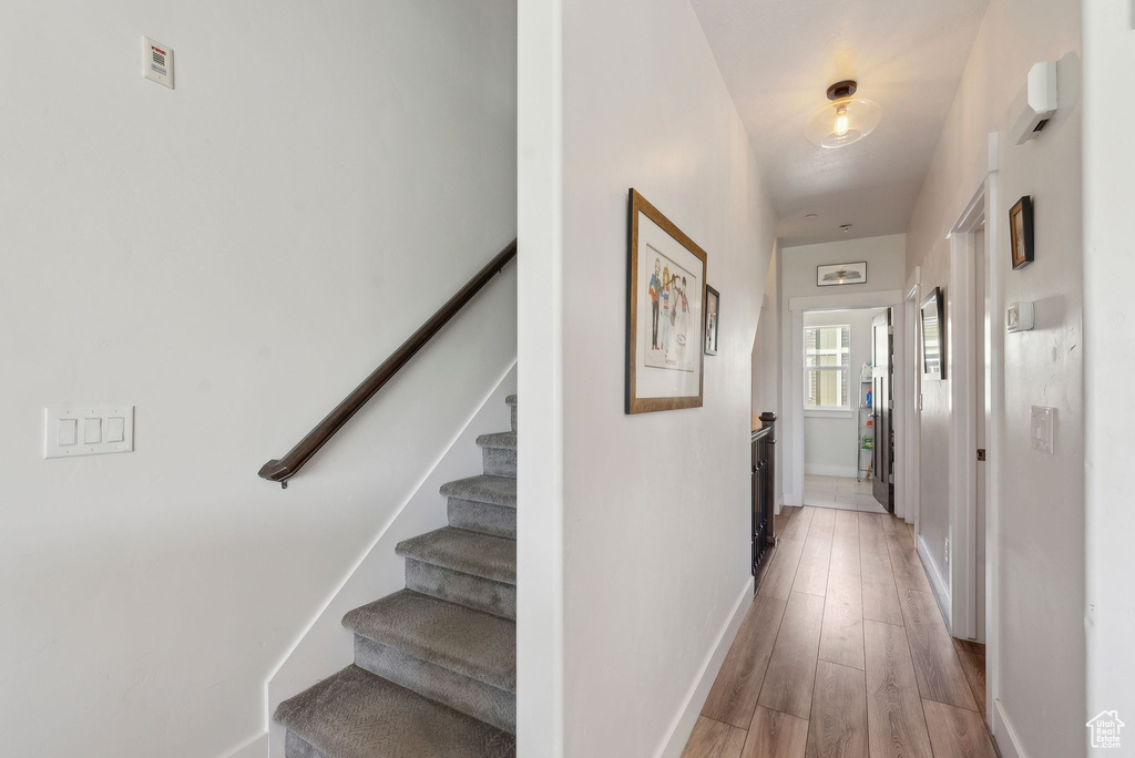 Corridor with stairway, baseboards, and light wood-style floors