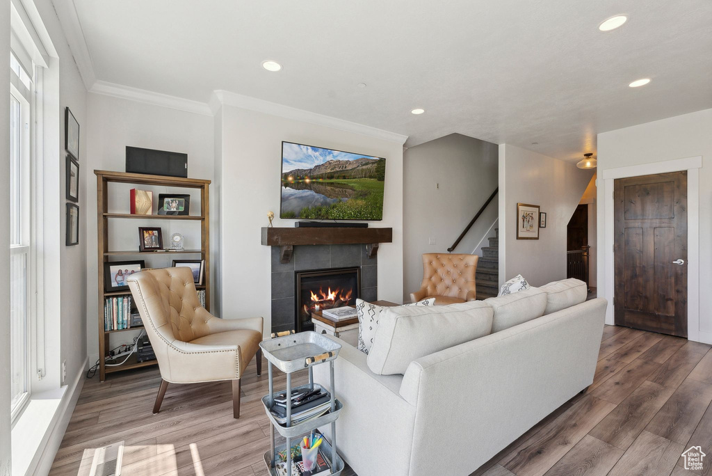 Living room with stairway, a tiled fireplace, wood finished floors, crown molding, and recessed lighting