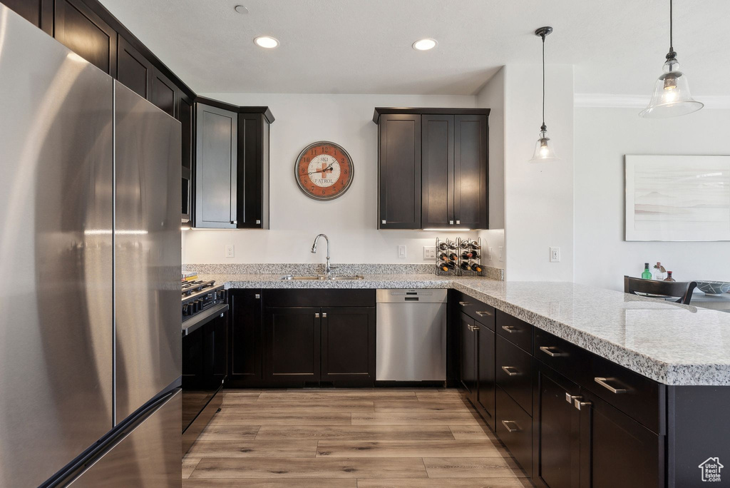 Kitchen featuring stainless steel appliances, a peninsula, a sink, light wood finished floors, and recessed lighting