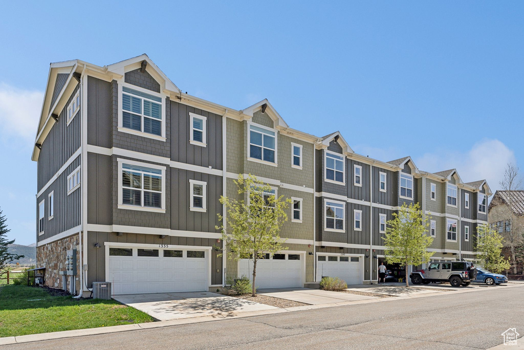 View of property featuring board and batten siding, a garage, cooling unit, a residential view, and driveway