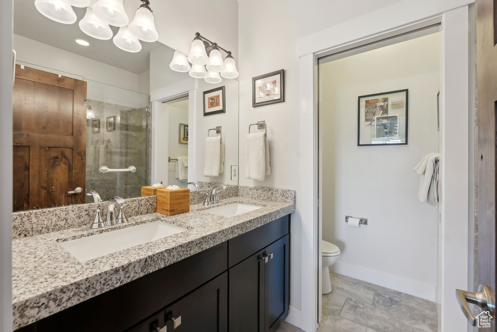 Bathroom featuring double vanity, toilet, baseboards, a tile shower, and a chandelier