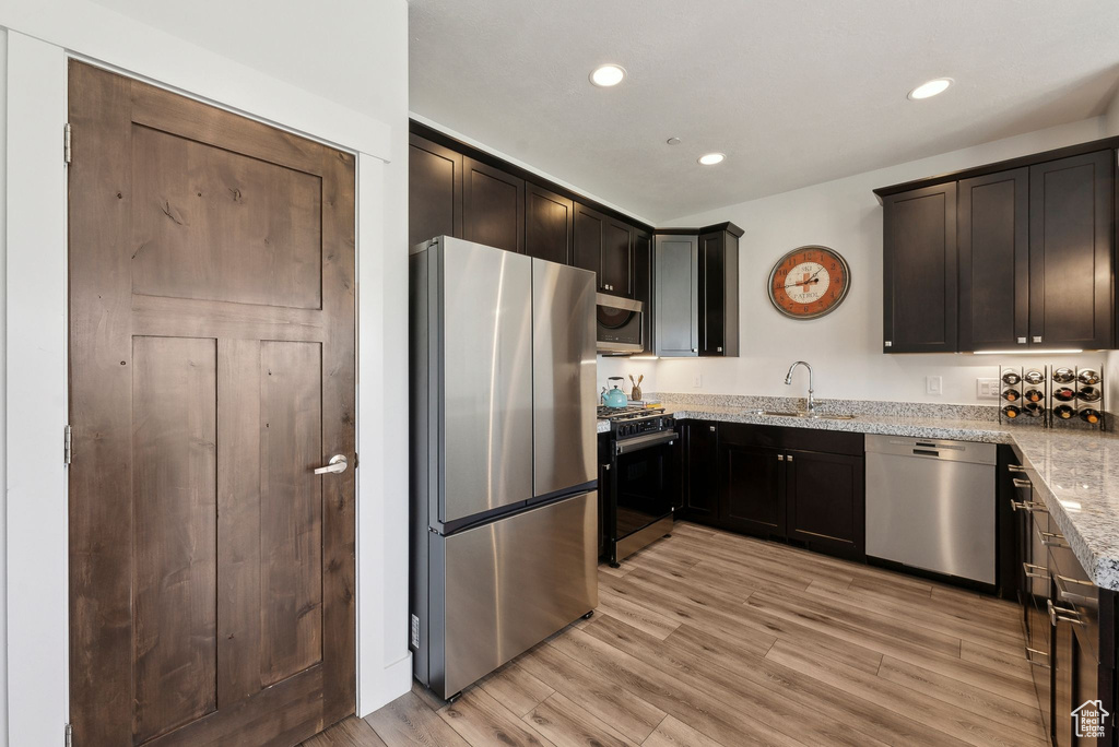 Kitchen with appliances with stainless steel finishes, a sink, light stone countertops, recessed lighting, and light wood-style flooring