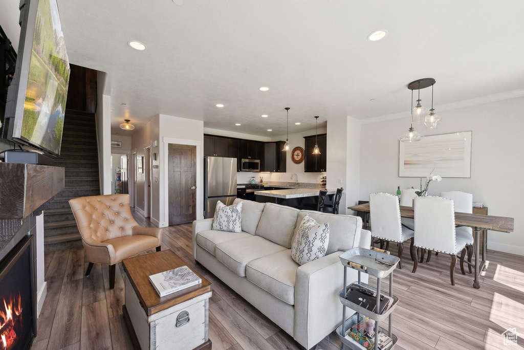 Living room featuring recessed lighting, light wood-style flooring, crown molding, baseboards, and stairs