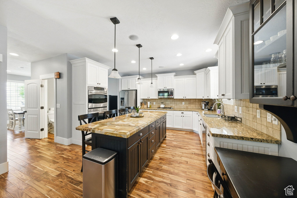Kitchen with stainless steel appliances, light wood-style flooring, white cabinets, backsplash, and recessed lighting