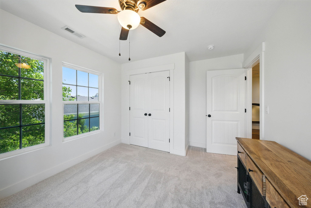 Unfurnished bedroom with light colored carpet, baseboards, ceiling fan, and a closet