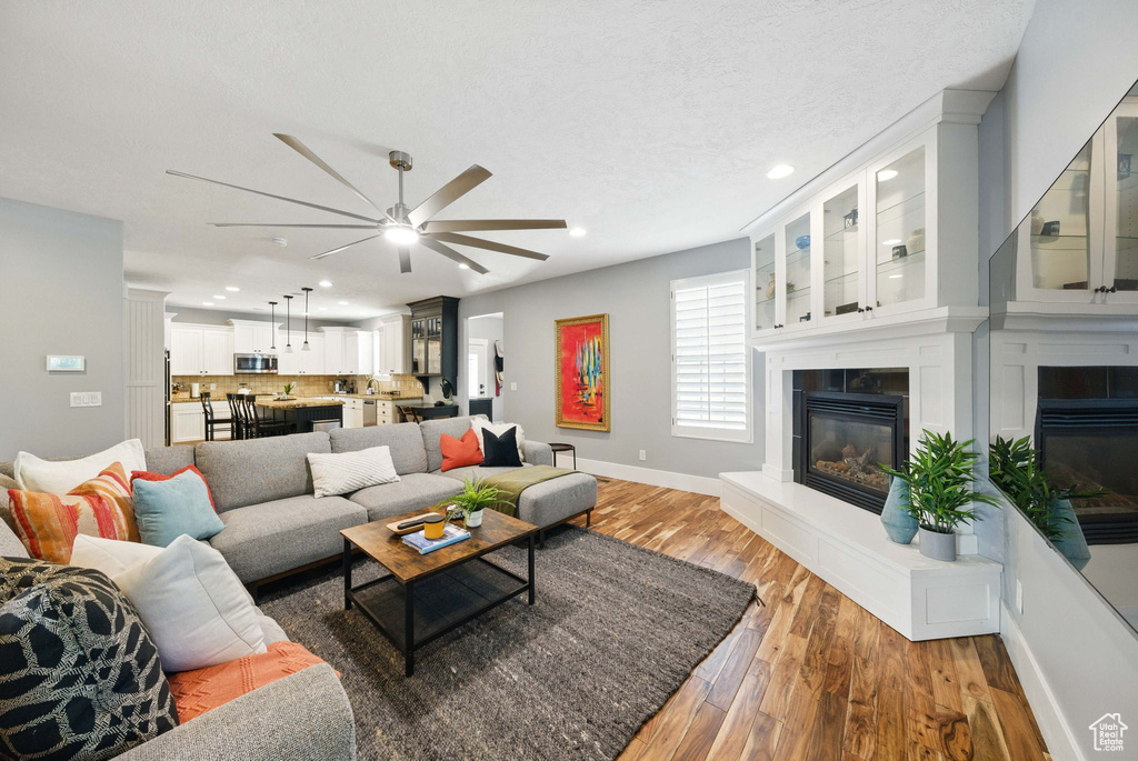 Living room featuring a fireplace, a ceiling fan, recessed lighting, light wood-style floors, and baseboards
