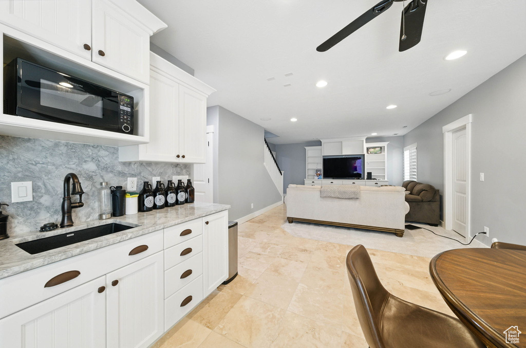 Kitchen featuring a sink, black microwave, a ceiling fan, tasteful backsplash, and white cabinetry