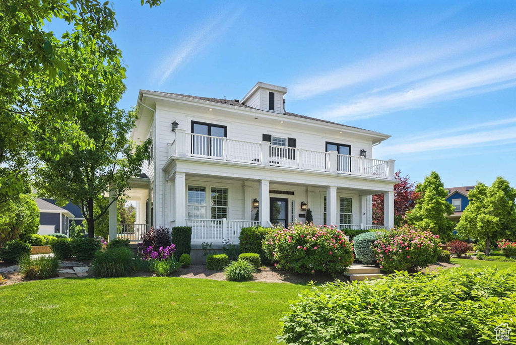 View of front of property featuring a balcony, a porch, and a front lawn