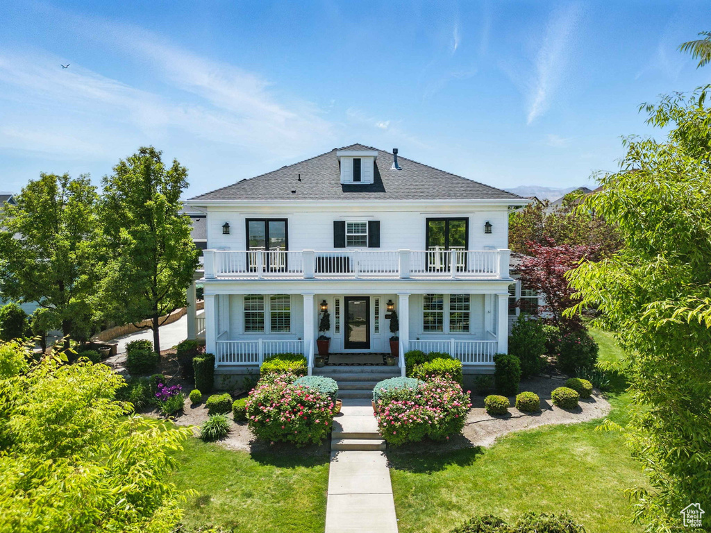 View of front of house featuring a balcony, covered porch, a front lawn, and roof with shingles