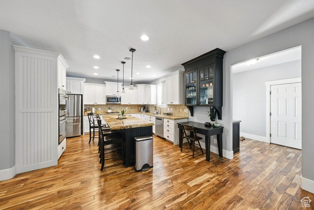 Kitchen featuring stainless steel appliances, light wood finished floors, a kitchen breakfast bar, a kitchen island, and decorative backsplash