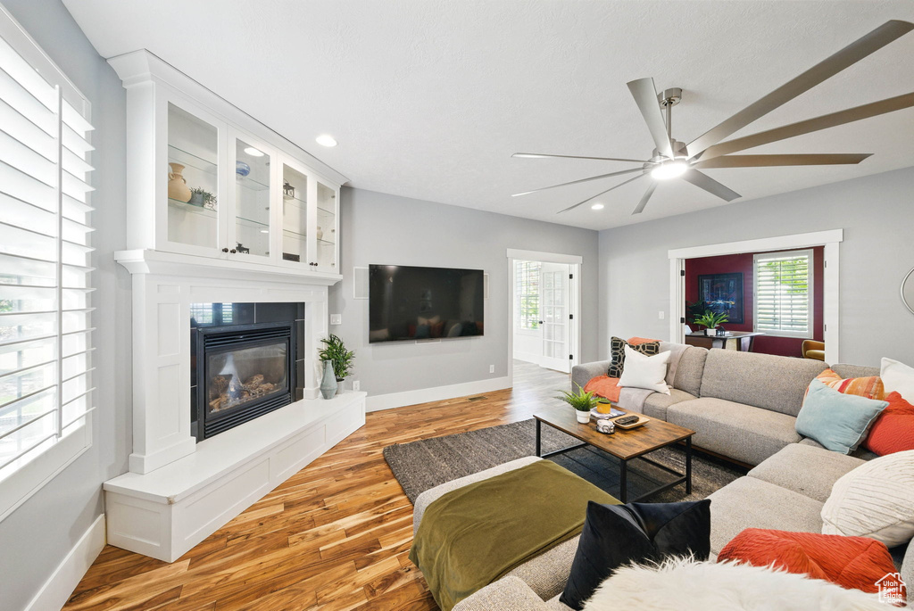 Living room featuring baseboards, light wood-type flooring, ceiling fan, recessed lighting, and a large fireplace