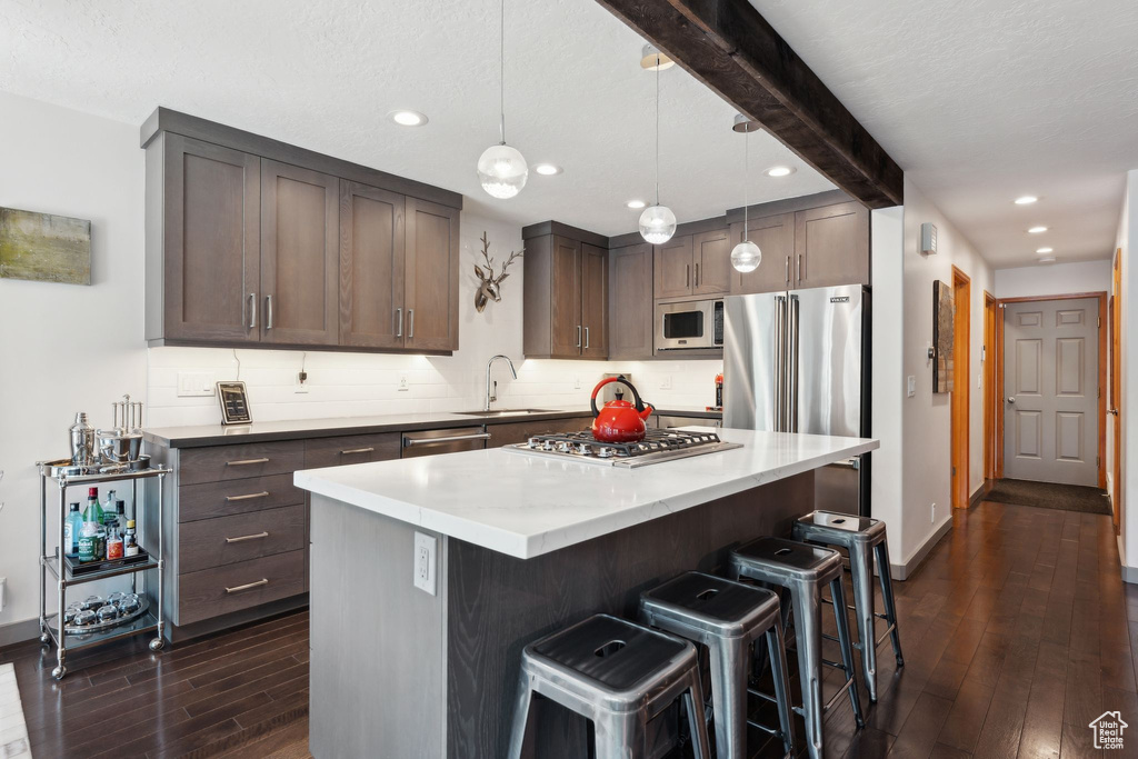 Kitchen with dark wood-style flooring, a sink, tasteful backsplash, appliances with stainless steel finishes, and a breakfast bar